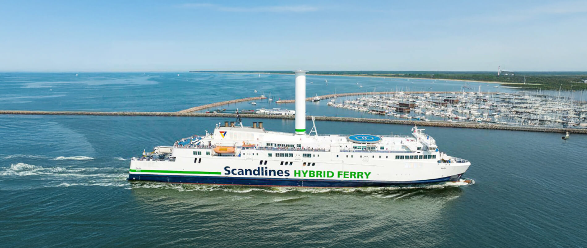 Eine Scandlines Hybridfähre fährt an einem Hafen entlang.