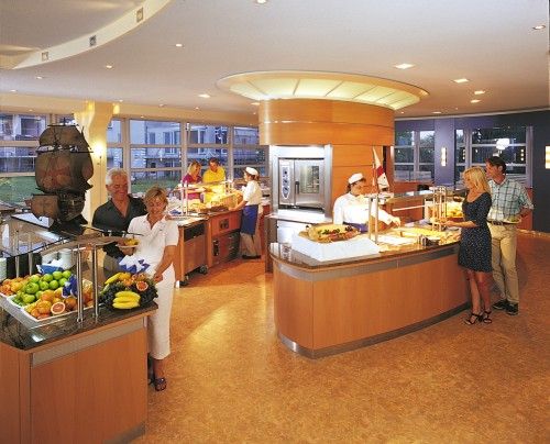 Menschen bedienen sich an einem Buffet in einem hellen, modernen Raum mit großen Fenstern.