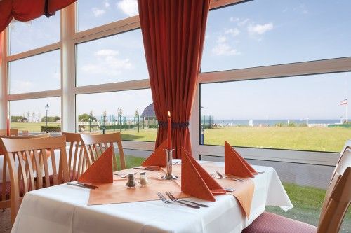 Ein elegant gedeckter Tisch in einem Restaurant am Fenster mit Blick auf eine Wiese und das Meer im Hintergrund.
