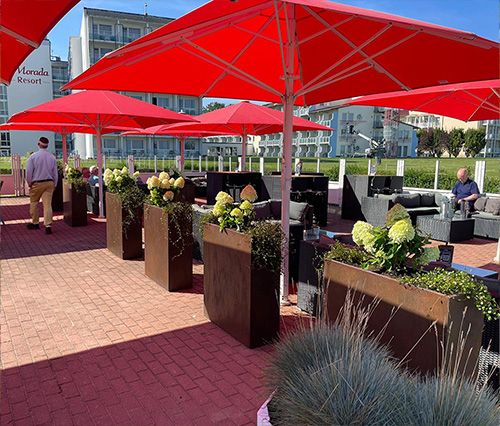 Außenterrasse eines Resorts mit roten Sonnenschirmen und Pflanzen in modernen Pflanzkübeln.