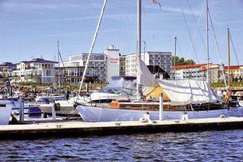 Segelboote im Hafen vor einem Resort mit mehreren Gebäuden im Hintergrund.