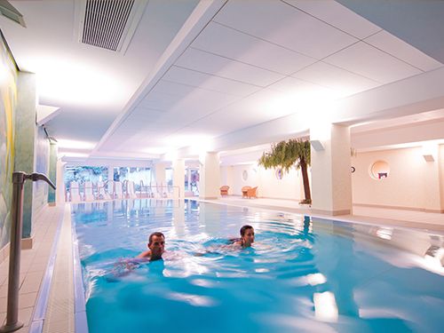 Zwei Personen schwimmen in einem hell erleuchteten Innenpool