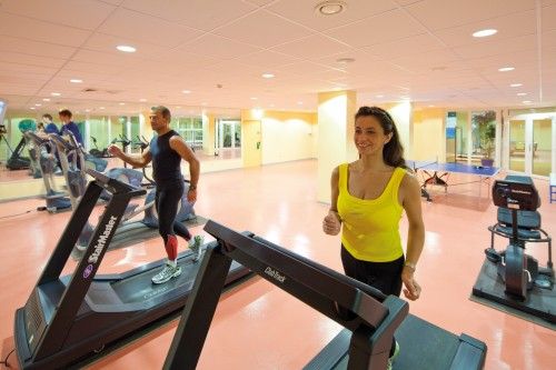 Zwei Personen trainieren auf Laufbändern in einem Fitnessstudio mit hellen Wänden und Spiegeln.