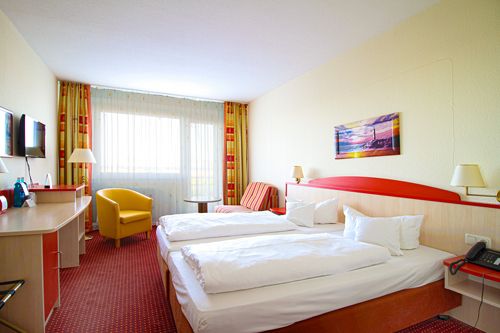 Hotelzimmer mit zwei Betten, gelbem Sessel, Schreibtisch und Fernseher.