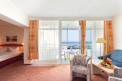 Helles Hotelzimmer mit Doppelbett, Balkon mit Meerblick, und gemütlicher Sitzecke.