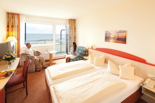 Hotelzimmer mit Doppelbett, Meerblick und zwei Personen, die sich unterhalten.