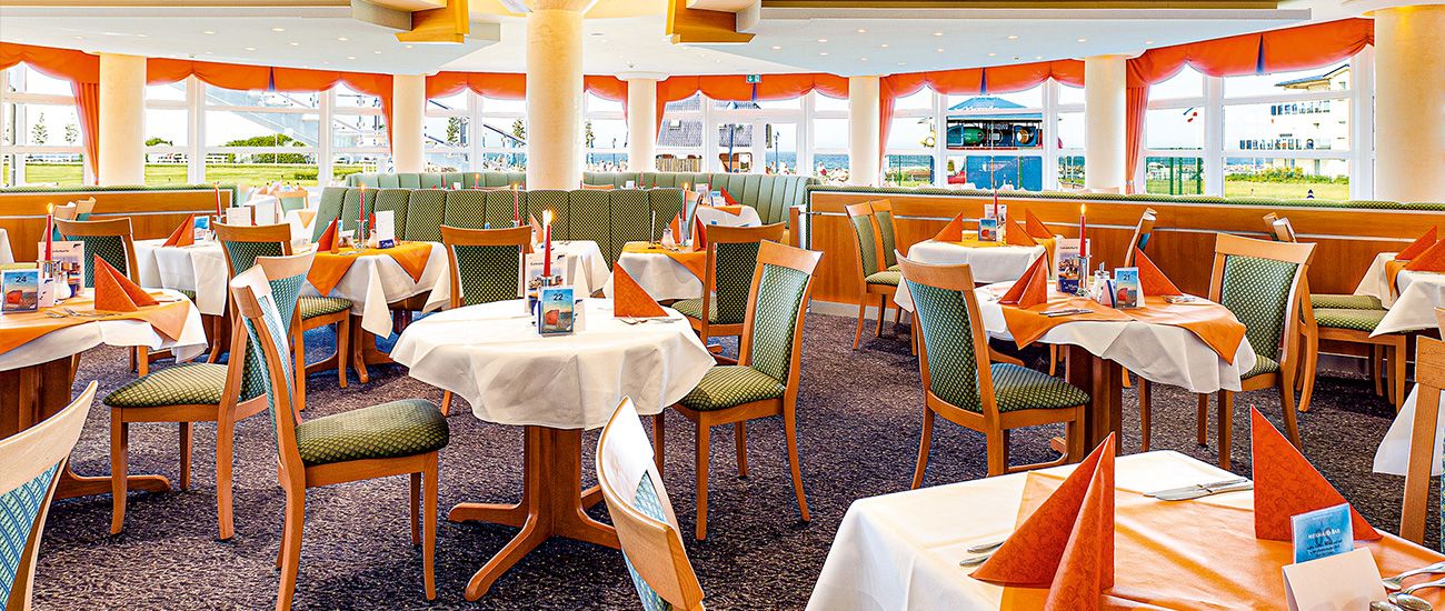 Helles und geräumiges Restaurant mit gedeckten Tischen und grünen Stühlen, orangen Akzenten und großen Fenstern.