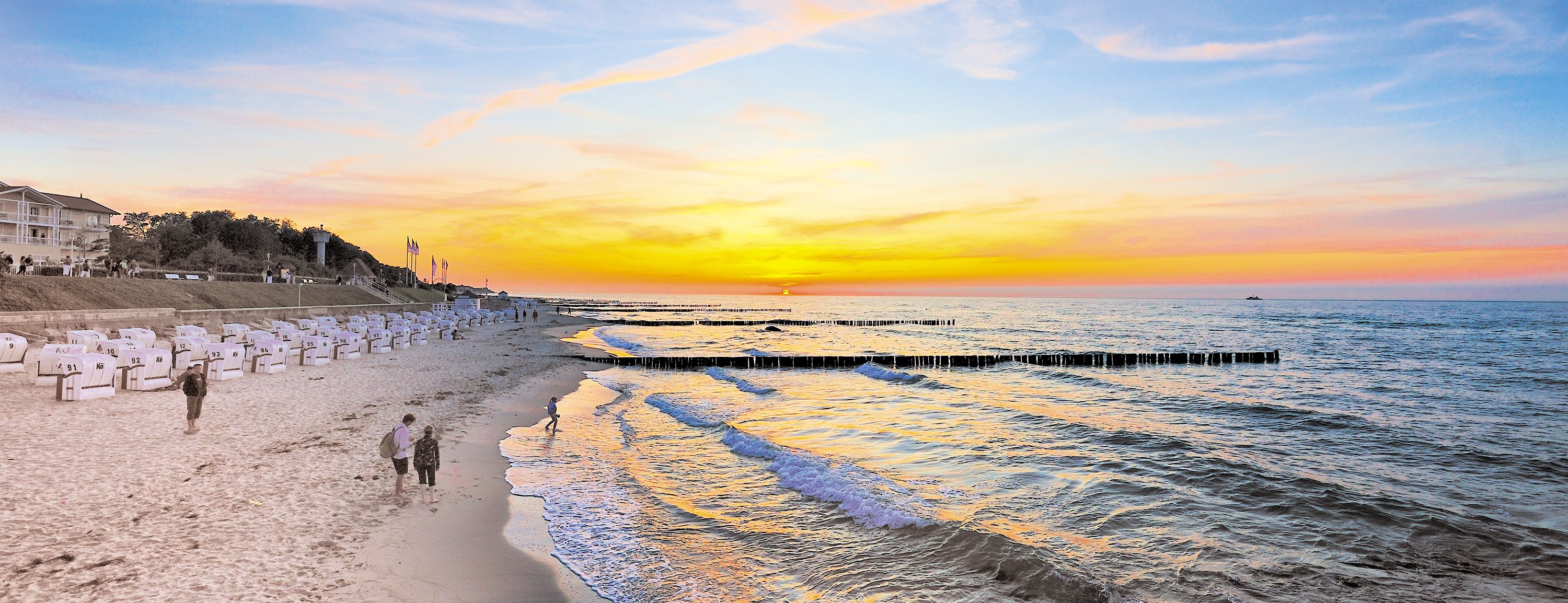 Strand mit Strandkörben und Personen im Sonnenuntergang, Wellen am Ufer