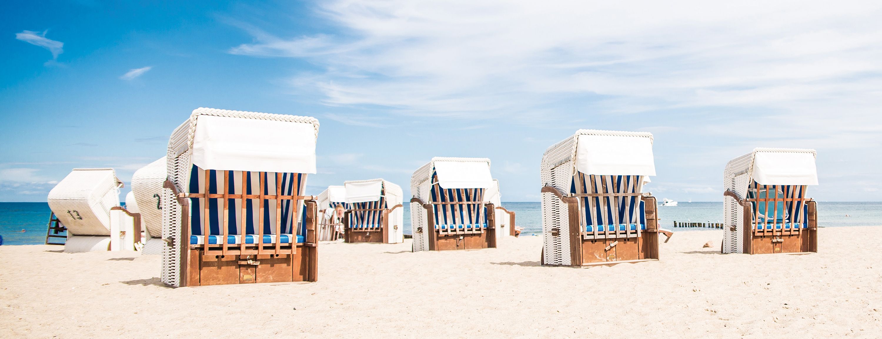 Strandkörbe stehen auf einem hellen Sandstrand vor blauem Meer und Himmel.