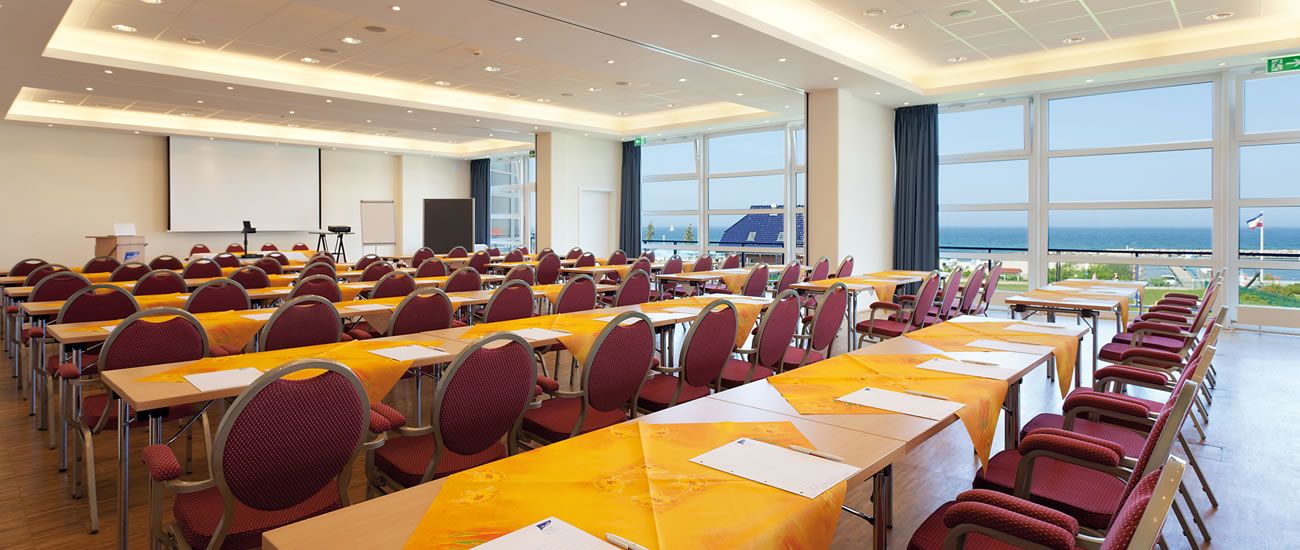 Konferenzraum mit Bestuhlung und Tischen, Blick auf das Meer durch große Fenster.