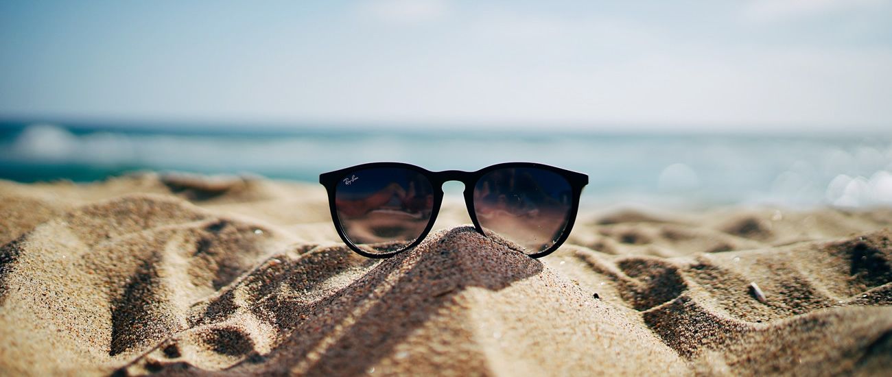Sonnenbrille im Sand am Strand mit unscharfem Meer im Hintergrund